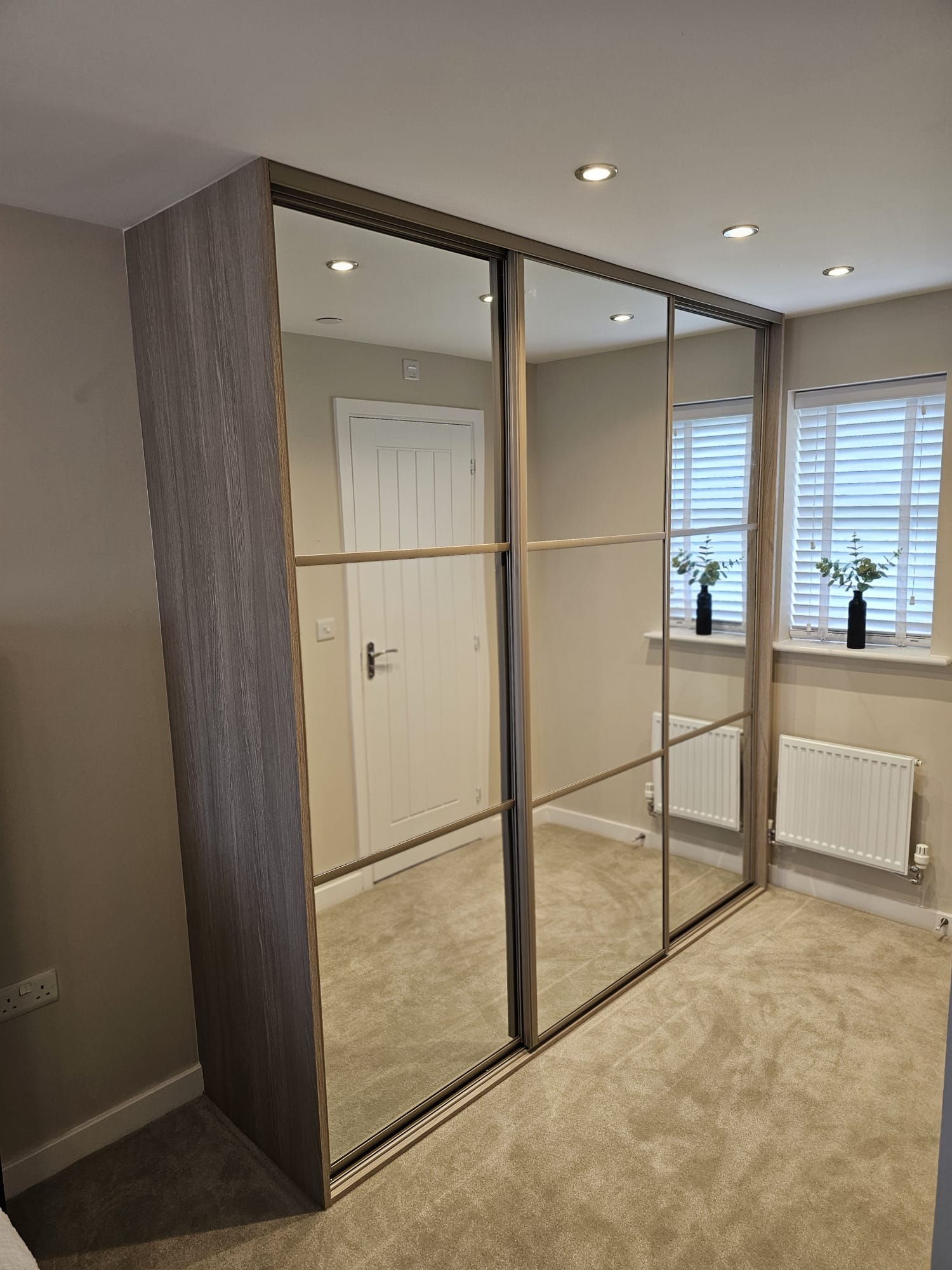 Three-door mirrored wardrobe fitted beside the windows in Newport