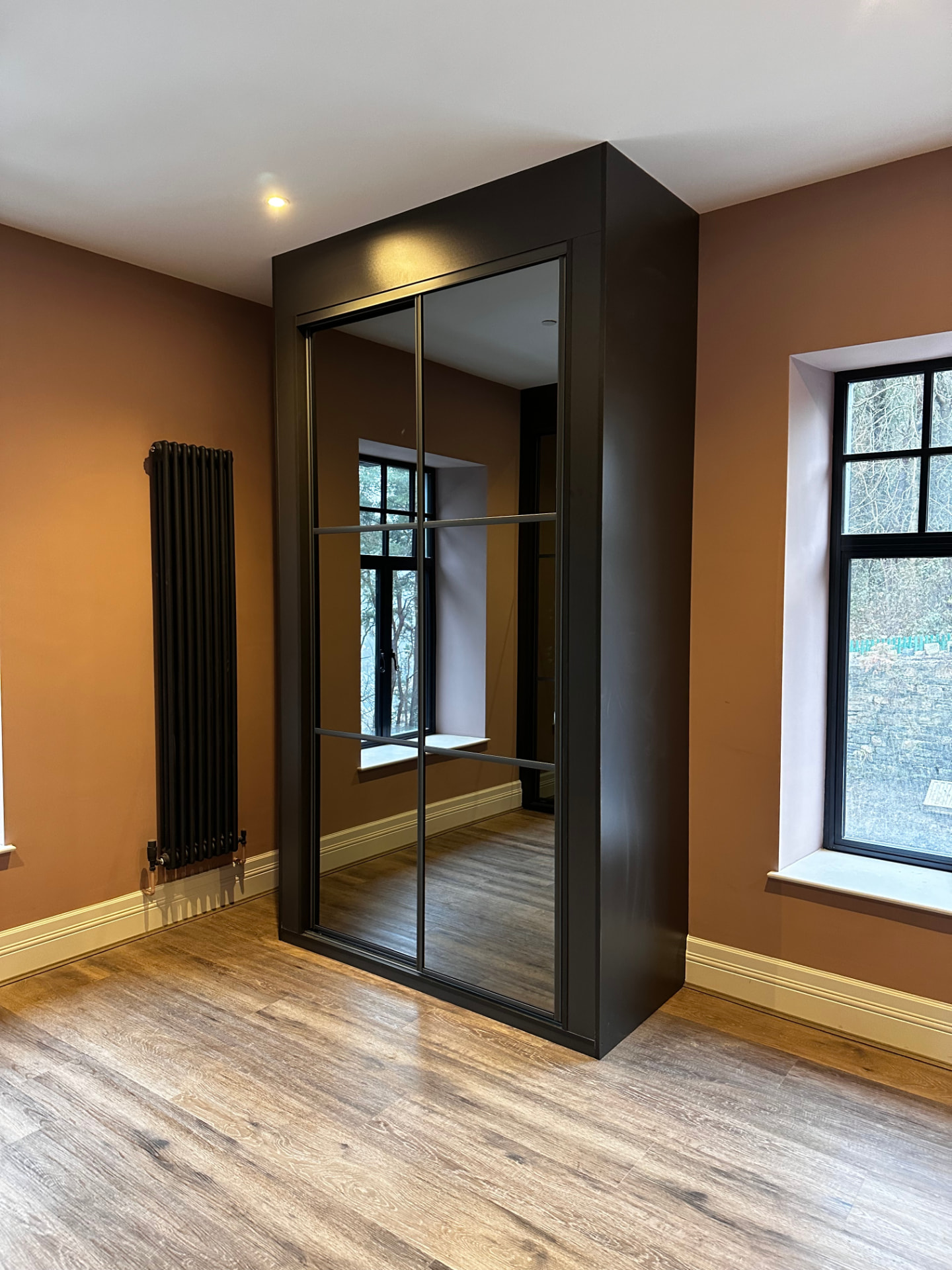 Two full-height mirror sliding doors with black frames and horizontal bars in a matching black surround in Carmarthen