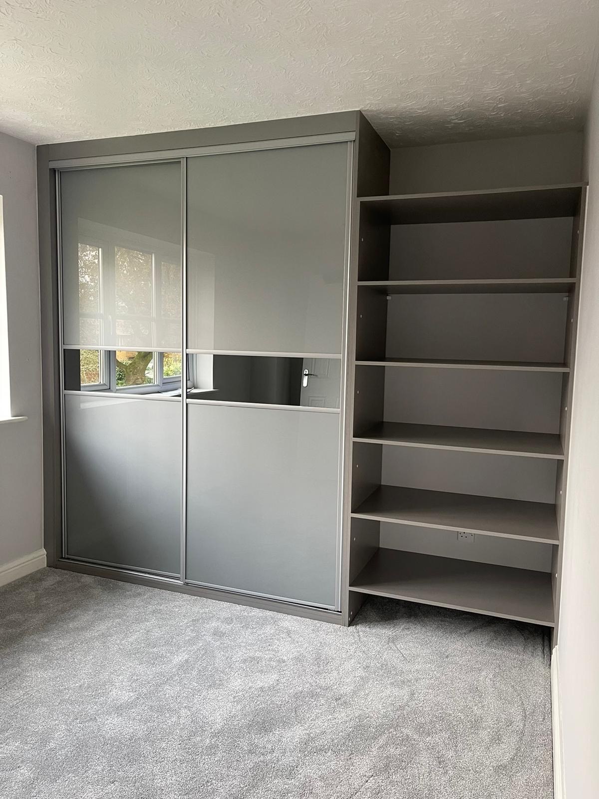 Grey coloured glass sliding doors with a central mirror band and matching open shelving in Cowbridge