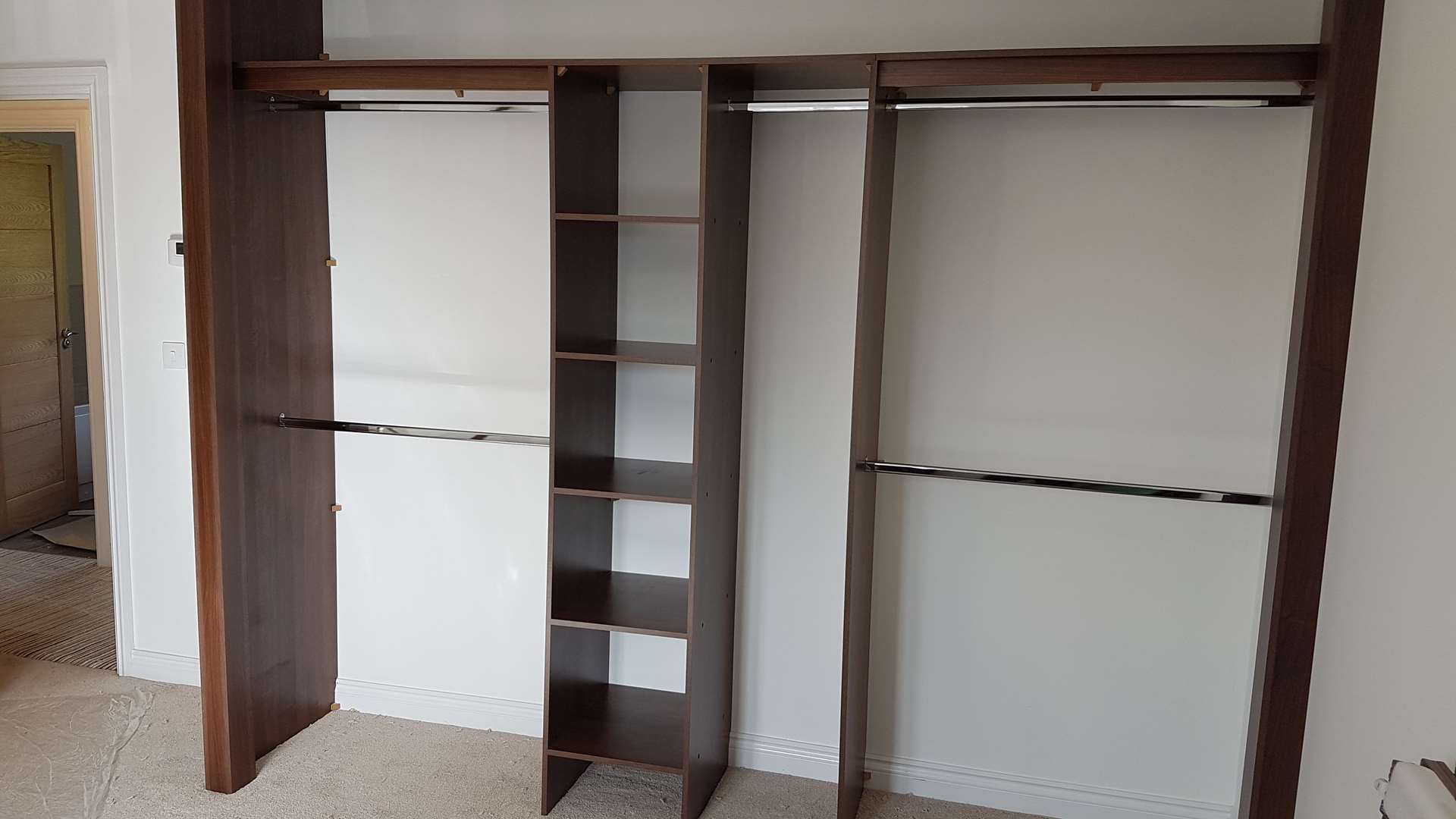 Walnut-effect wardrobe interior with single and double hanging rails either side of a central shelf tower, before the doors go on in Cwm