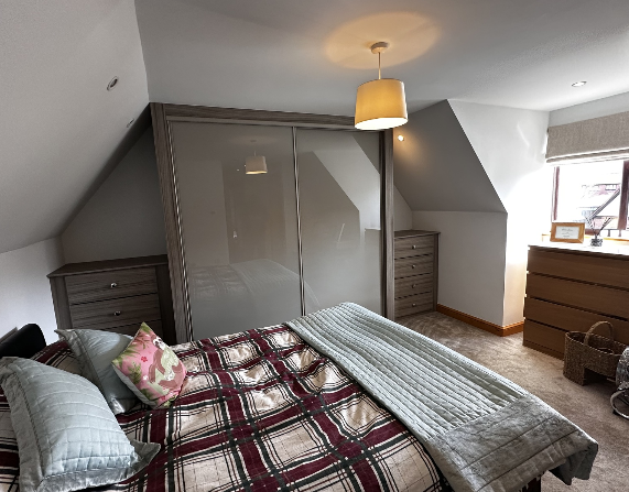 Two grey coloured glass sliding doors in a dark wood-grain surround, with matching drawer units beneath sloping ceilings in Carmarthen