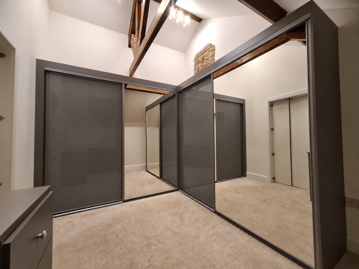 Dark grey coloured glass sliding doors in a corner run beneath a vaulted ceiling in Port Talbot