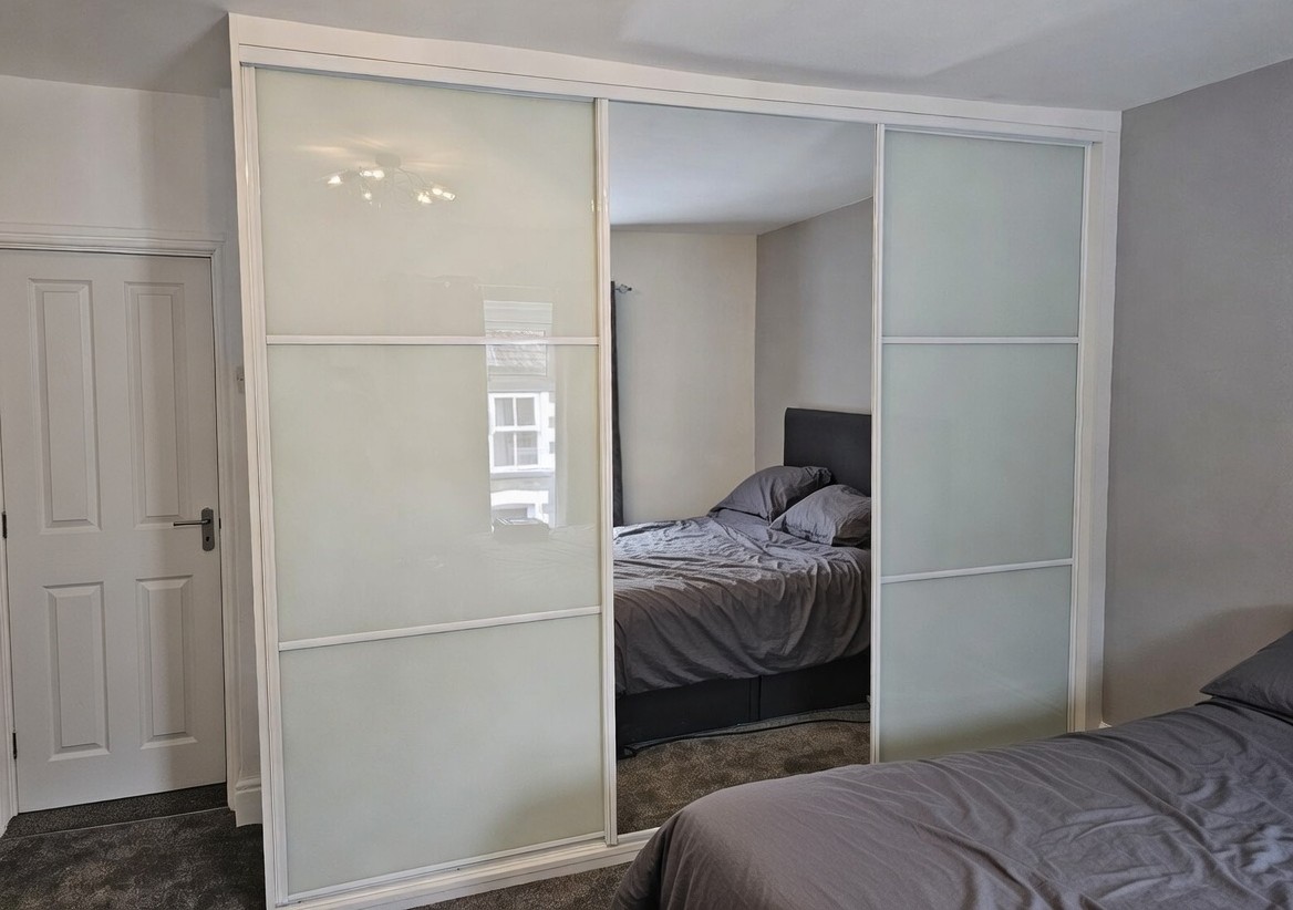 White-framed sliding doors with pale coloured glass side panels, horizontal divisions and a full-height central mirror in Carmarthen